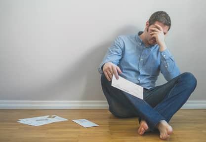 Very upset man sitting at the floor with bills.