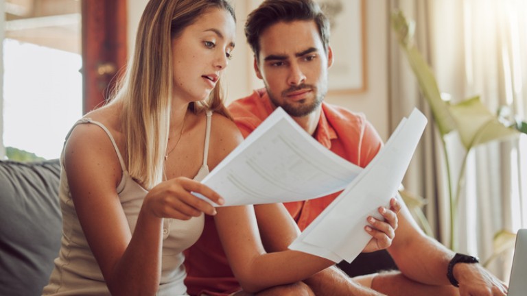 Budget, debt and mortgage with a couple reading bills and documents while checking their expenses and savings. Husband and wife looking worried while reading a loan application or contract together