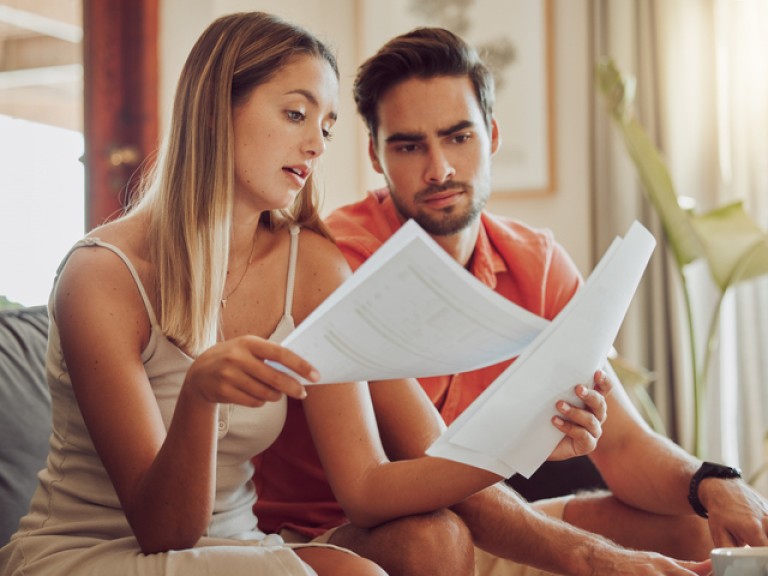 Budget, debt and mortgage with a couple reading bills and documents while checking their expenses and savings. Husband and wife looking worried while reading a loan application or contract together