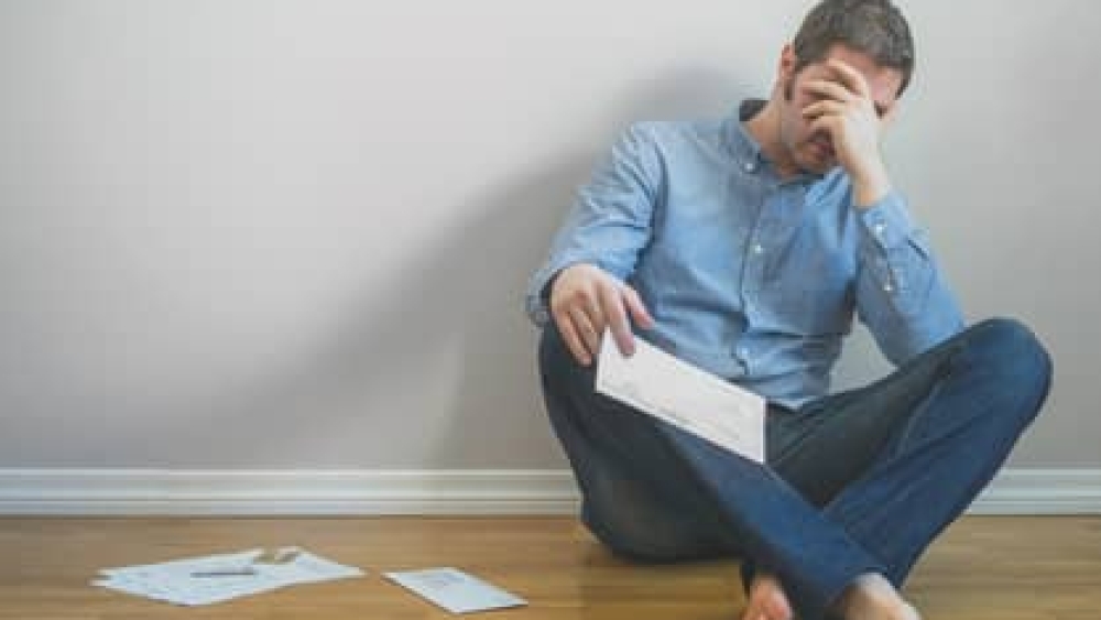 Very upset man sitting at the floor with bills.