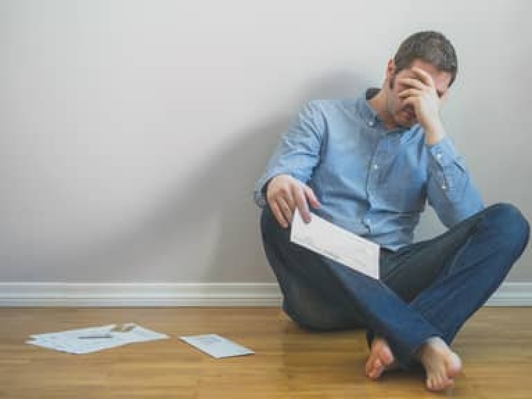 Very upset man sitting at the floor with bills.