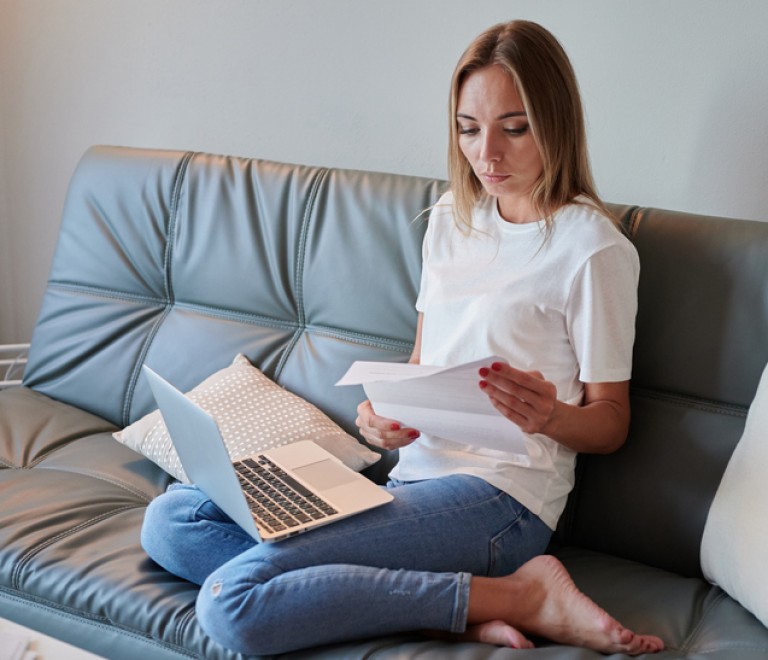 Young female with laptop on the couch reading eviction letter