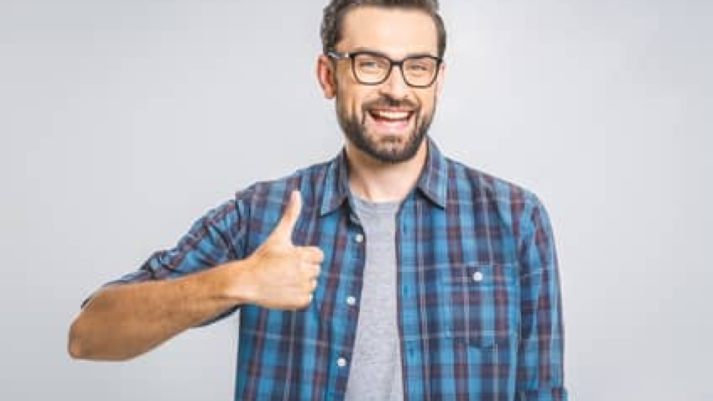 Happy young man. Portrait of handsome young man smiling while standing against white background. Thumbs up.