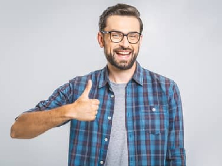 Happy young man. Portrait of handsome young man smiling while standing against white background. Thumbs up.