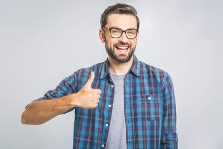 Happy young man. Portrait of handsome young man smiling while standing against white background. Thumbs up.