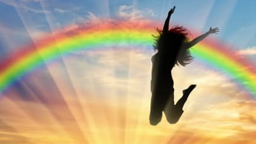 Happy woman jumping near rainbow