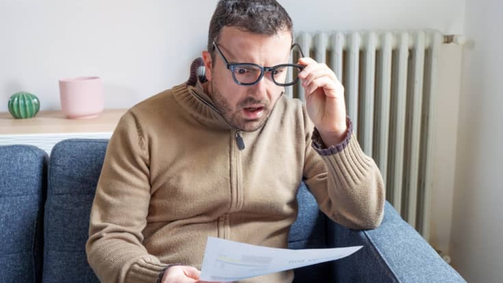 Shocked man reading some bills energy expenses on sofa living room