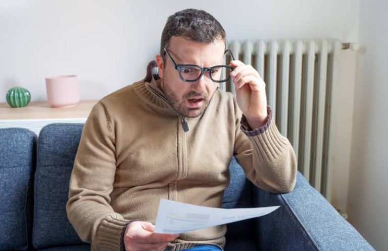 Shocked man reading some bills energy expenses on sofa living room