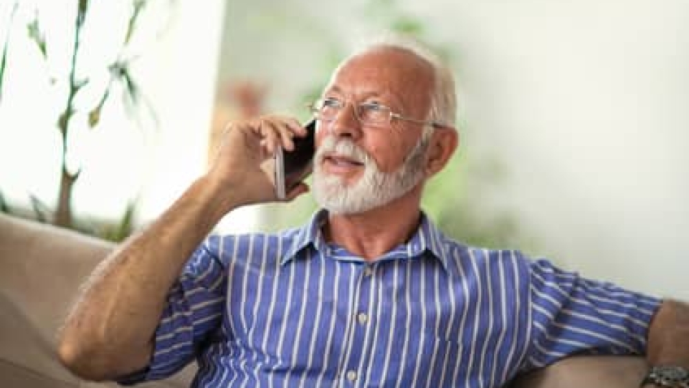 Senior man chatting on a mobile phone while relaxing on a sofa in his living room