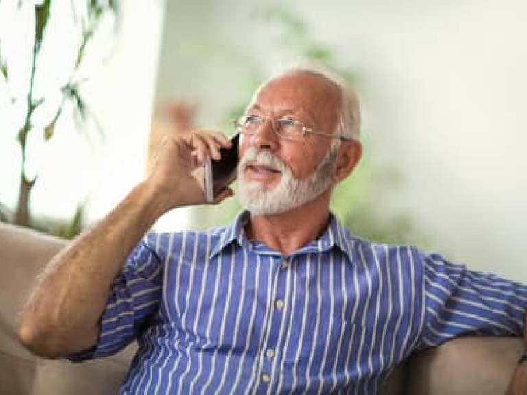 Senior man chatting on a mobile phone while relaxing on a sofa in his living room