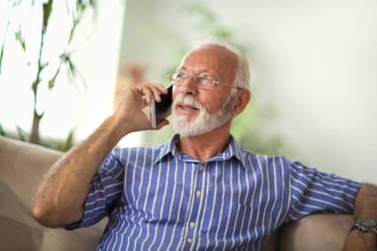 Senior man chatting on a mobile phone while relaxing on a sofa in his living room