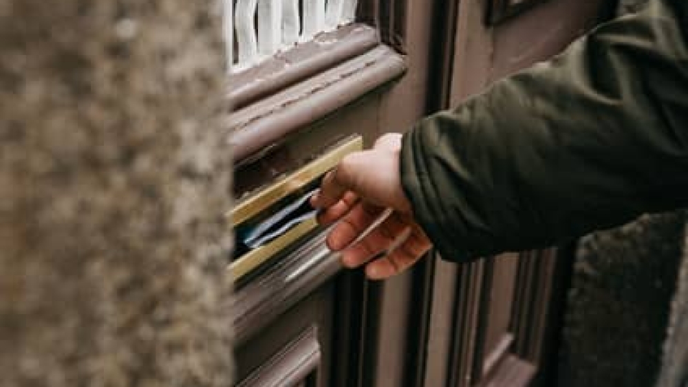 Close-up. The postman puts a letter or newspaper or magazine in the mailbox at the door of a residential building or a person puts a brochure with advertising