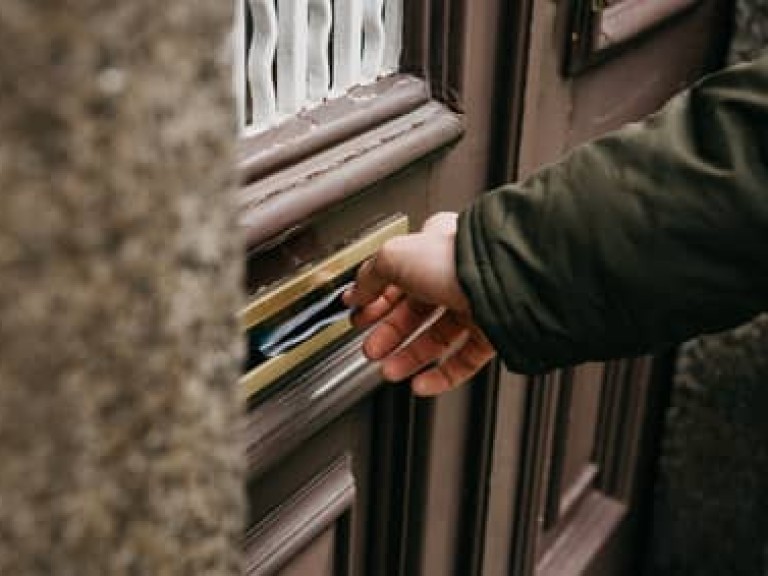 Close-up. The postman puts a letter or newspaper or magazine in the mailbox at the door of a residential building or a person puts a brochure with advertising